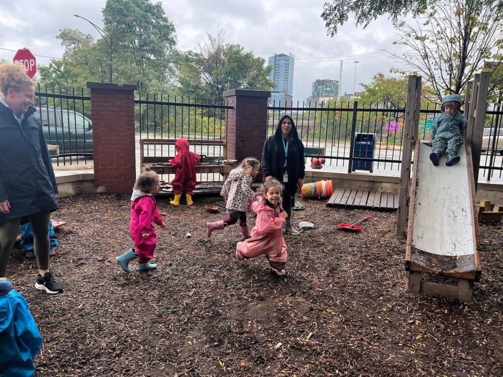 Smiling students run through the garden, one can be seen going down a slide