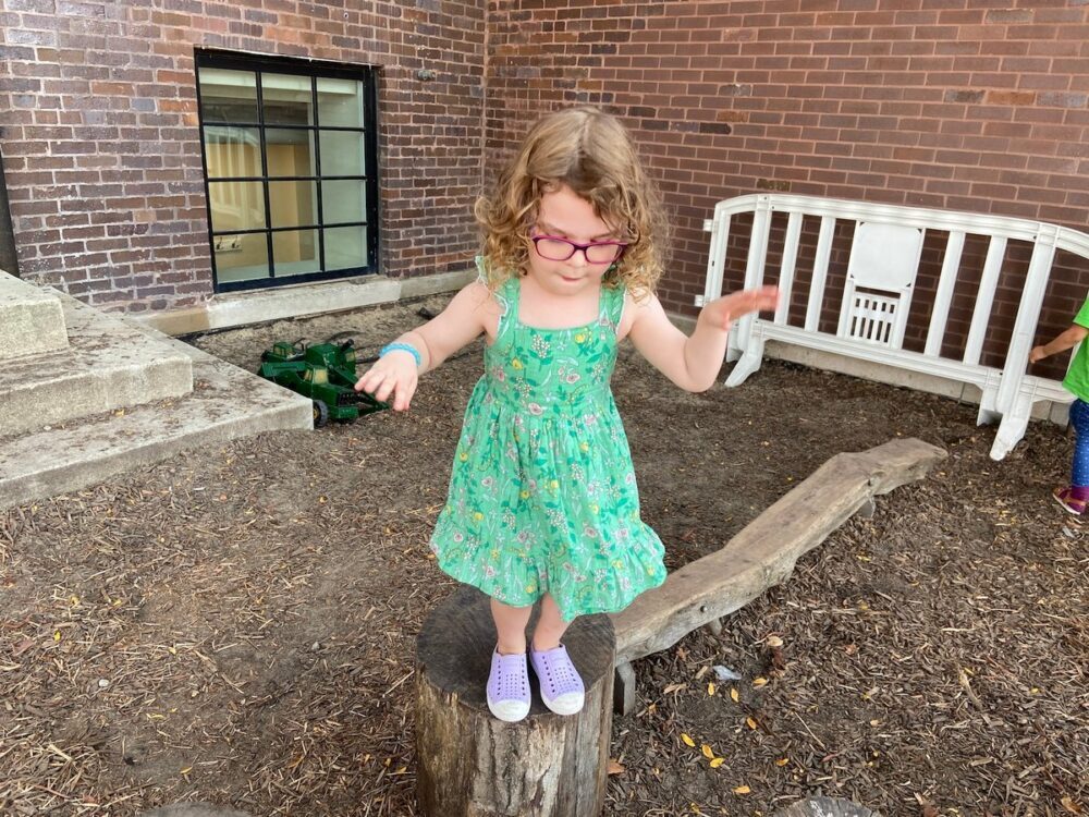 Early childhood student balances on a log in the garden, possibly preparing to jump off